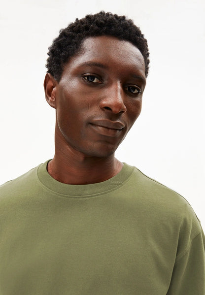 Close-up of the crew neck and textured jersey on the ARMEDANGELS Canada Maarkos Heavy Weight T-Shirt in fatigue green, worn by a man.