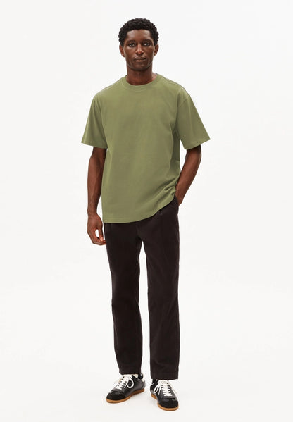 Full-length view of a man wearing the ARMEDANGELS Canada Maarkos Heavy Weight T-Shirt in fatigue green with black trousers and loafers on a white background.