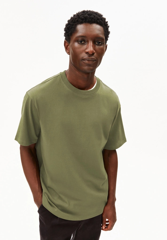 Man wearing the ARMEDANGELS Canada Maarkos Heavy Weight T-Shirt in fatigue green with black trousers, front view on a white background.