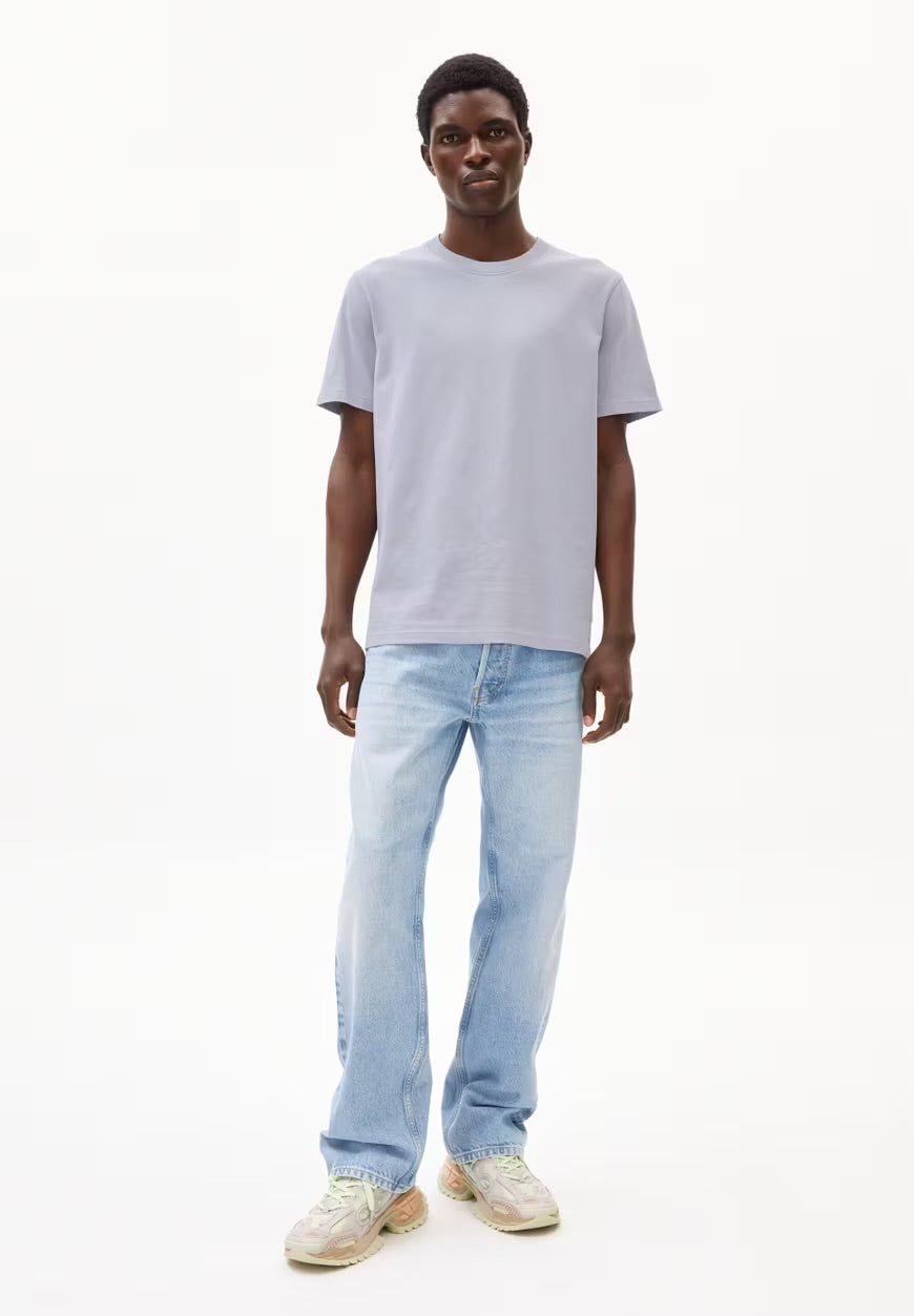 Full-length view of a man wearing the ARMEDANGELS Canada Maarkos Heavy Weight T-Shirt in misty morning light grey-blue with light-wash jeans and sneakers on a white background.