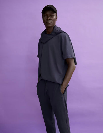 Man in a black cap wearing the ARMEDANGELS Canada Maarkos Heavy Weight T-Shirt in night sky under a navy hoodie against a lilac backdrop.