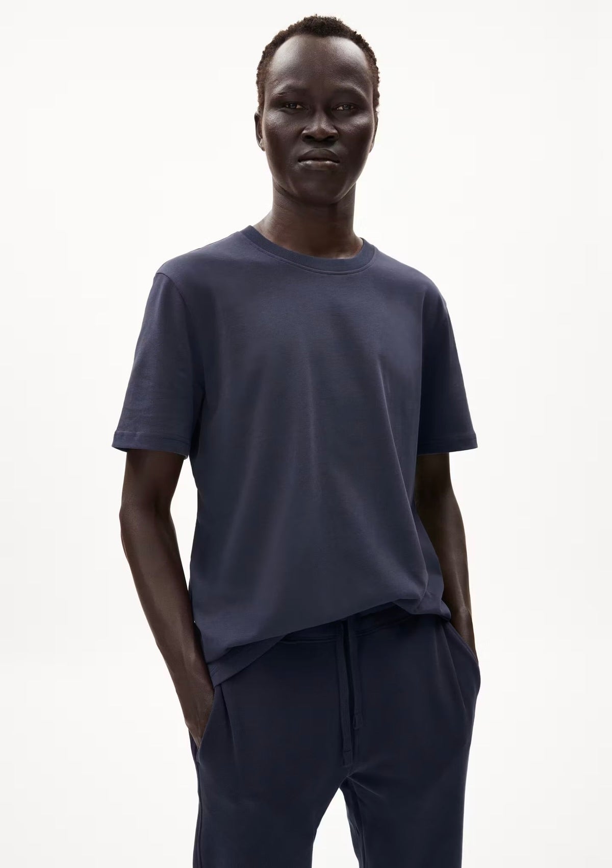Man wearing the ARMEDANGELS Canada Maarkos Heavy Weight T-Shirt in night sky navy with navy trousers, front view on a white background.