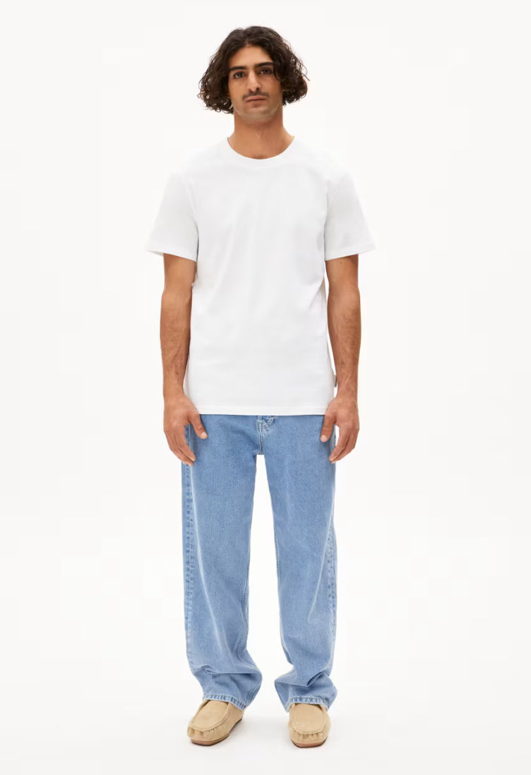 Full-length view of a man wearing the ARMEDANGELS Canada Maarkos Heavy Weight T-Shirt in white with light-wash jeans and beige shoes on a white background.