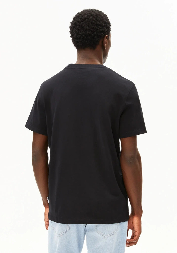 A man viewed from behind wearing a plain black short-sleeve t-shirt and light blue jeans against a white studio background.