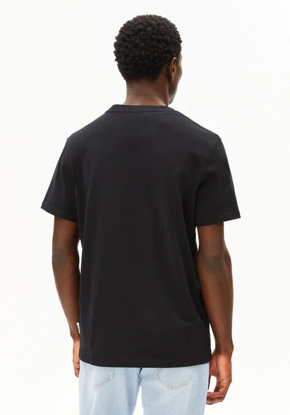 A man viewed from behind wearing a plain black short-sleeve t-shirt and light blue jeans against a white studio background.