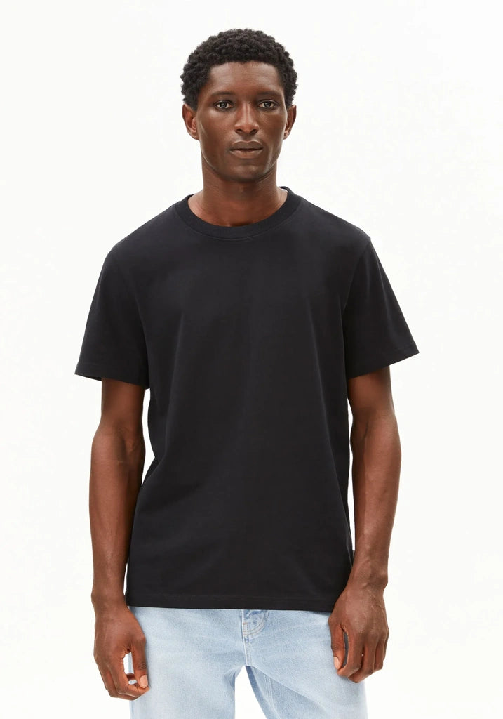 A man wearing a plain black short-sleeve crewneck t-shirt and light blue jeans, standing against a solid white background.