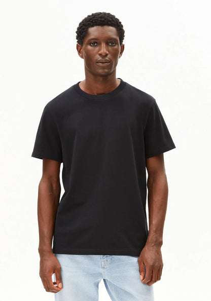 A man wearing a plain black short-sleeve crewneck t-shirt and light blue jeans, standing against a solid white background.