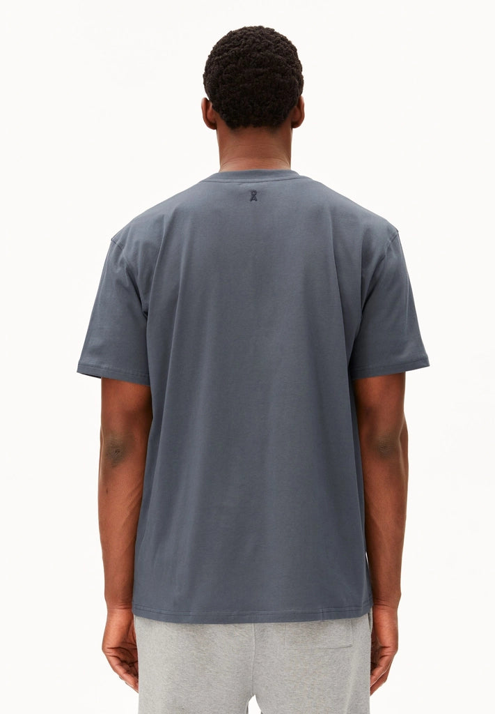 Back view of a man wearing the ARMEDANGELS Canada Maarkos Mid Weight T-Shirt in moonshadow with grey sweatpants on a white background.