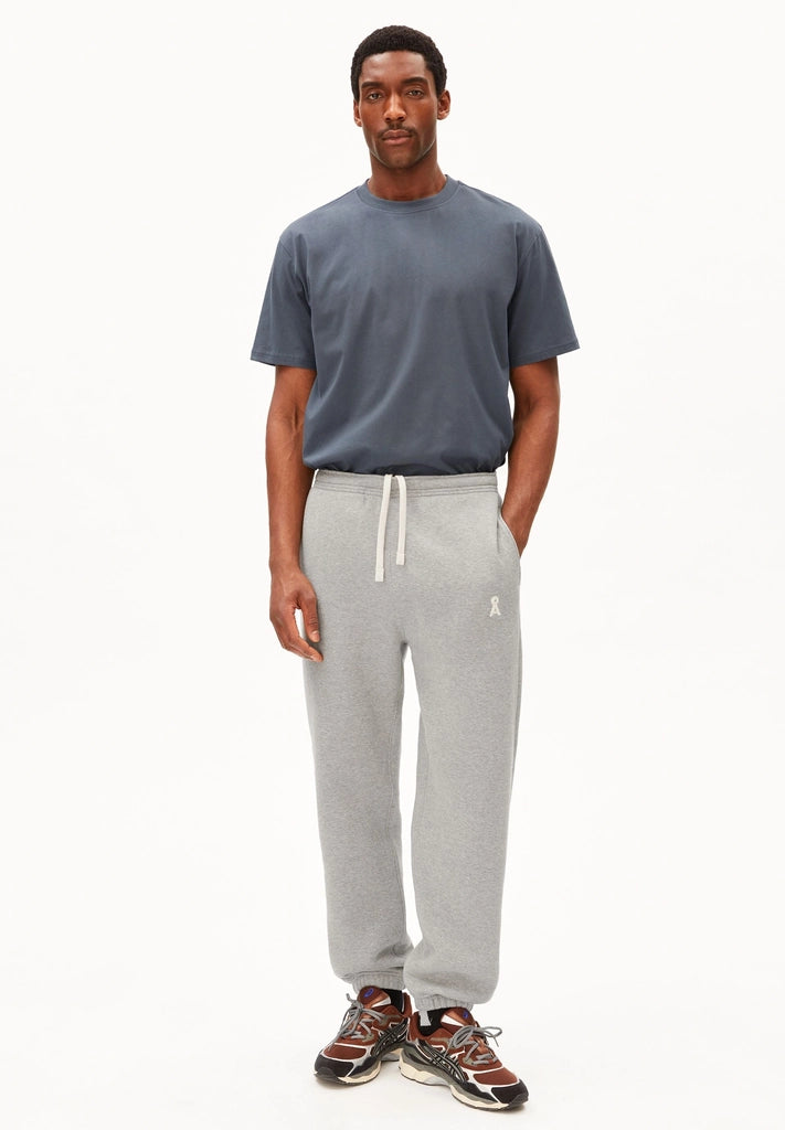 Full-length view of a man wearing the ARMEDANGELS Canada Maarkos Mid Weight T-Shirt in moonshadow with grey sweatpants and trail sneakers on a white background.