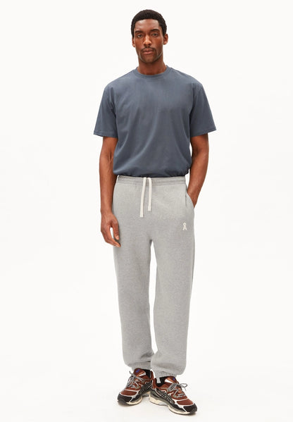 Full-length view of a man wearing the ARMEDANGELS Canada Maarkos Mid Weight T-Shirt in moonshadow with grey sweatpants and trail sneakers on a white background.
