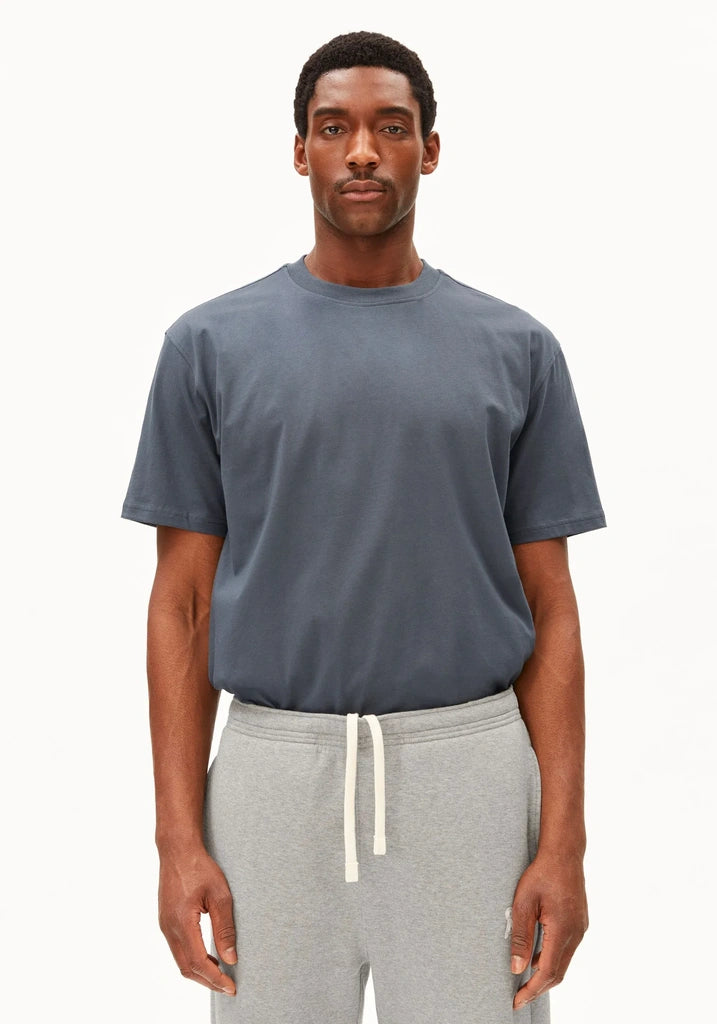 Man wearing the ARMEDANGELS Canada Maarkos Mid Weight T-Shirt in moonshadow grey-blue with grey drawstring sweatpants, front view on a white background.