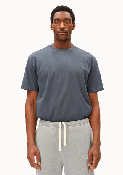 Man wearing the ARMEDANGELS Canada Maarkos Mid Weight T-Shirt in moonshadow grey-blue with grey drawstring sweatpants, front view on a white background.