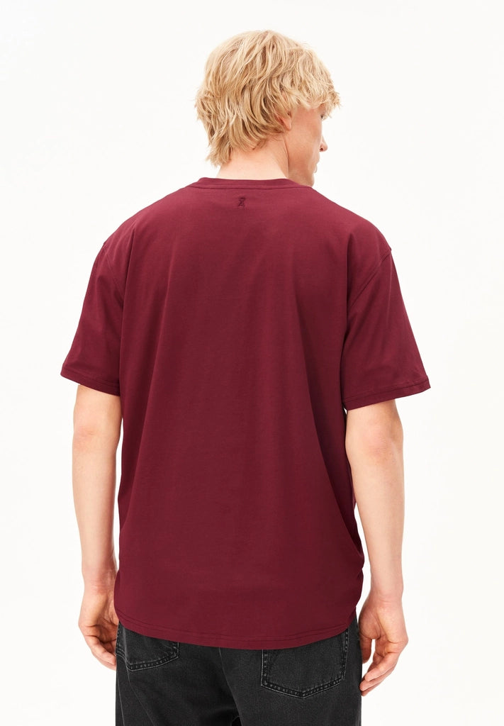 Back view of a man wearing the ARMEDANGELS Canada Maarkos Mid Weight T-Shirt in velvet red with black jeans on a white background.
