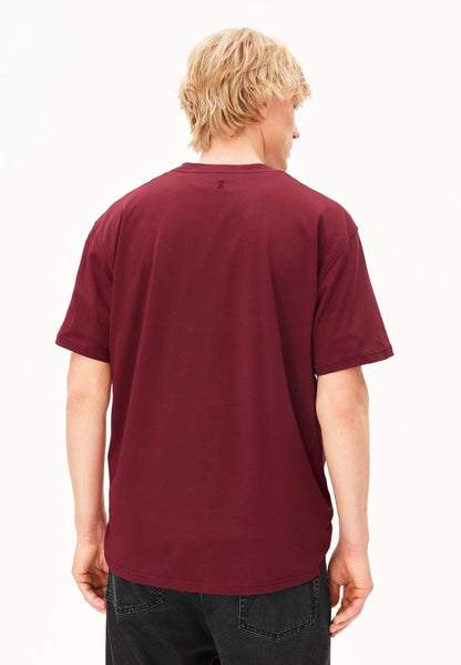 Back view of a man wearing the ARMEDANGELS Canada Maarkos Mid Weight T-Shirt in velvet red with black jeans on a white background.