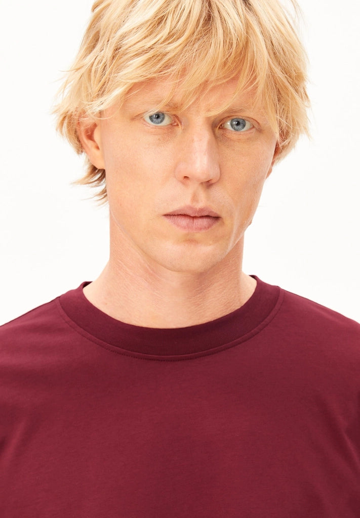 Close-up of the crew neckline on the ARMEDANGELS Canada Maarkos Mid Weight T-Shirt in velvet red, worn by a man.