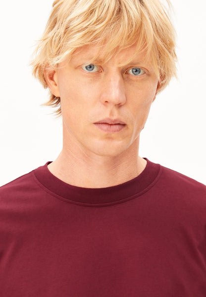 Close-up of the crew neckline on the ARMEDANGELS Canada Maarkos Mid Weight T-Shirt in velvet red, worn by a man.