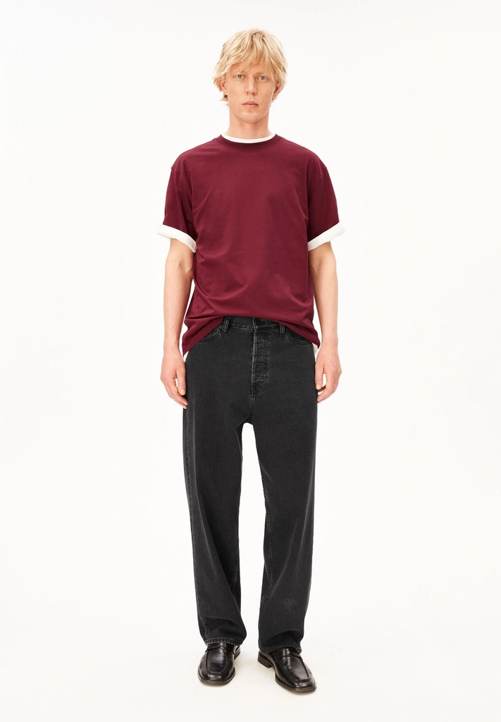 Full-length view of a man wearing the ARMEDANGELS Canada Maarkos Mid Weight T-Shirt in velvet red over a white tee with black jeans and black shoes on a white background.