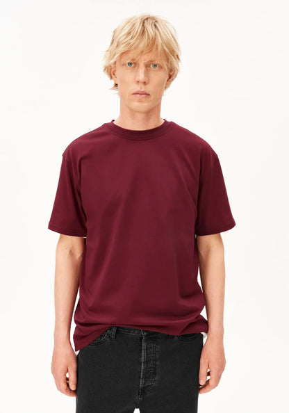 Man wearing the ARMEDANGELS Canada Maarkos Mid Weight T-Shirt in velvet red with black jeans, front view on a white background.