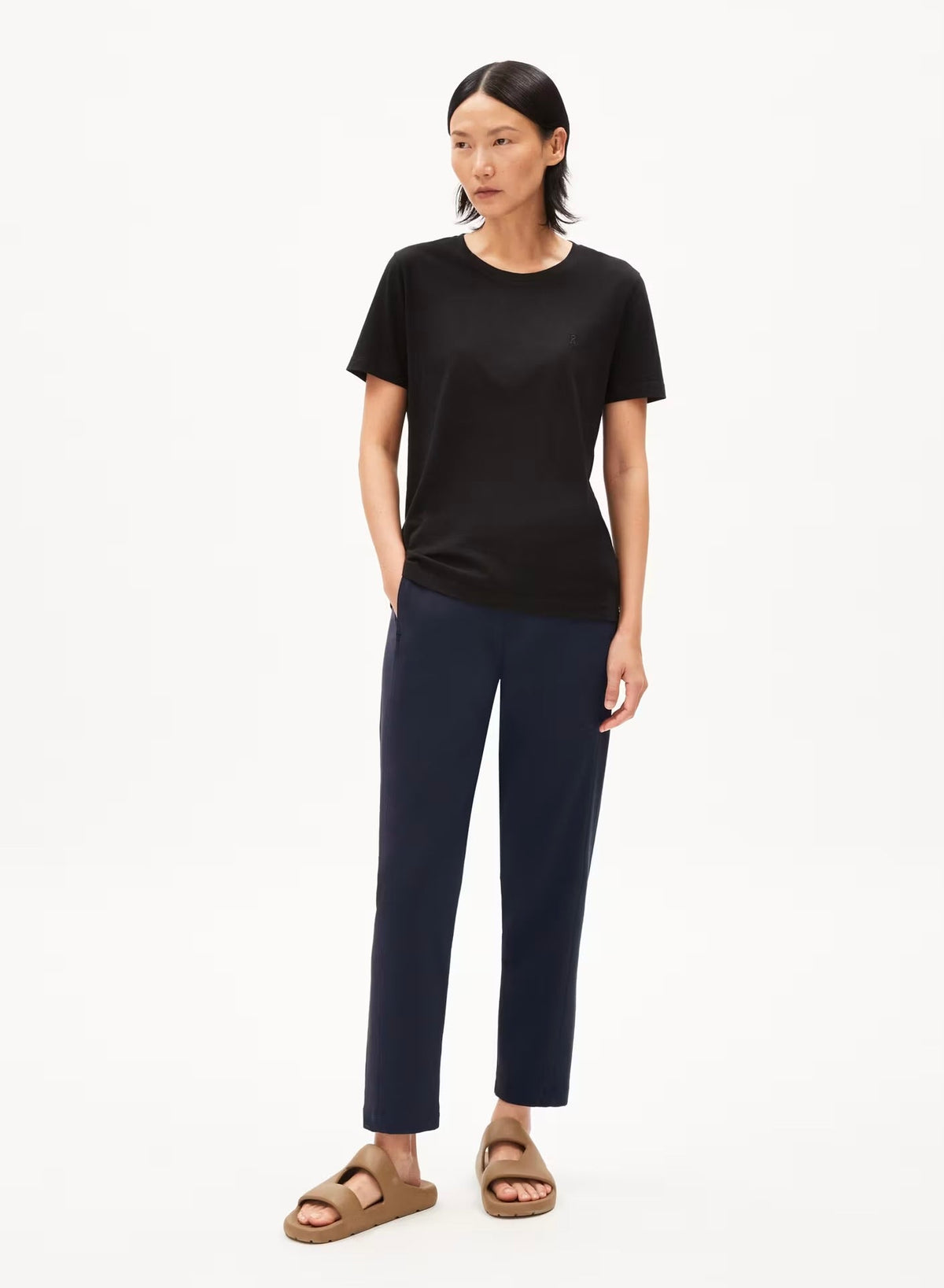 Woman wearing the ARMEDANGELS Canada Magdaalena Jersey Pant in night sky navy with a black tee and tan sandals, against a white studio background.