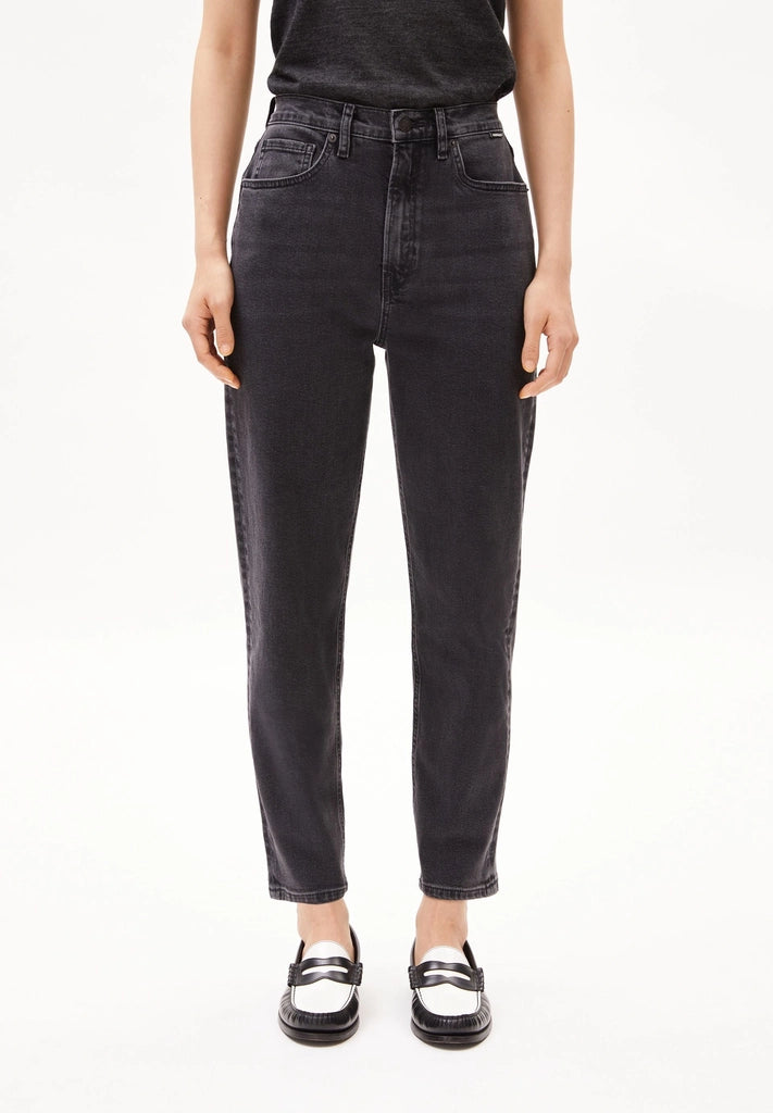 Woman wearing ARMEDANGELS Canada Mairaa mom jeans in black with a black tee and white and black loafers on a white background.
