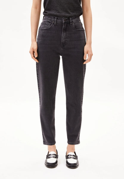 Woman wearing ARMEDANGELS Canada Mairaa mom jeans in black with a black tee and white and black loafers on a white background.