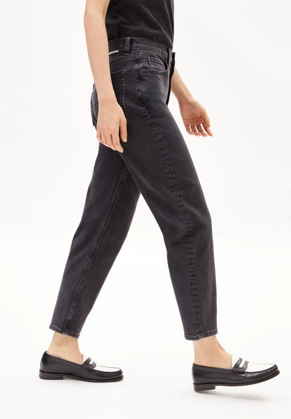 Side view of a woman walking in ARMEDANGELS Canada Mairaa tapered ankle-length mom jeans in black with loafers.