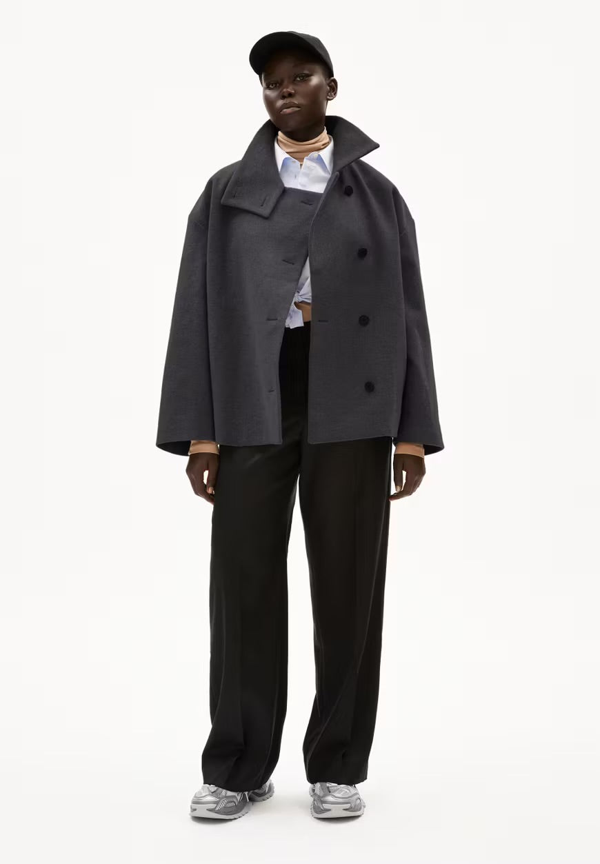 Full-length view of a woman wearing ARMEDANGELS Canada Majelaa wool coat in steel melange grey, open over a striped shirt with black trousers and silver sneakers.