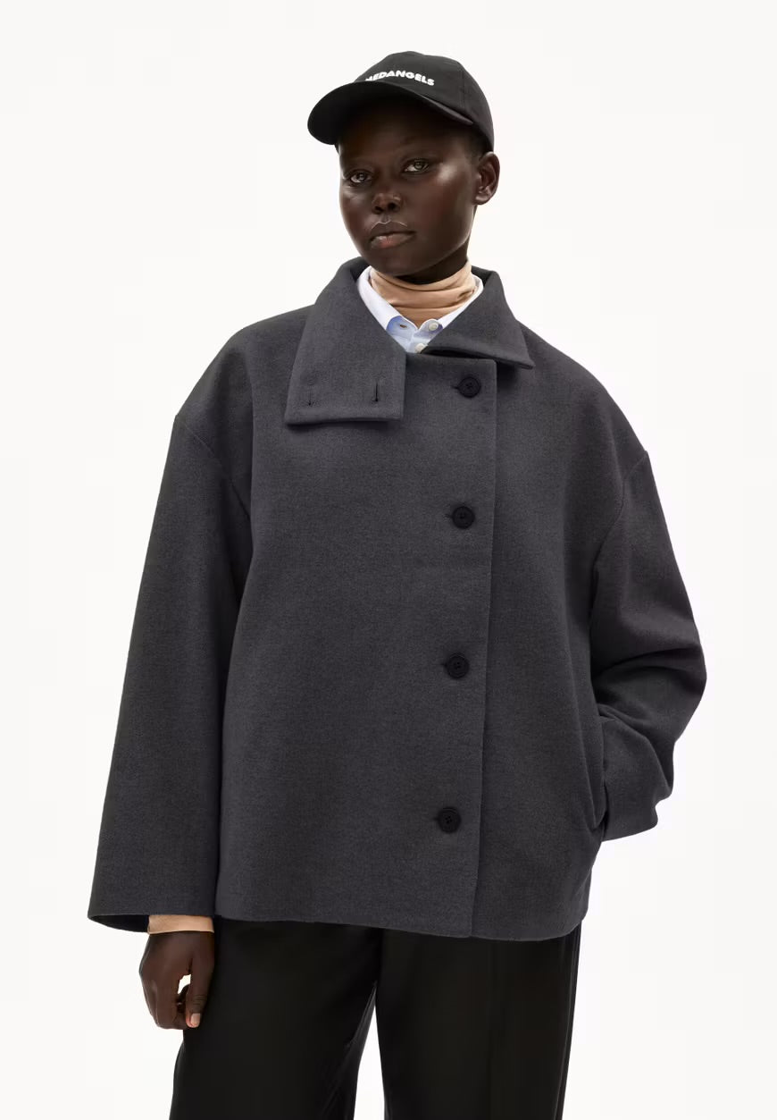 Woman wearing ARMEDANGELS Canada Majelaa cropped wool coat in steel melange grey with a black cap and black trousers on a white background.