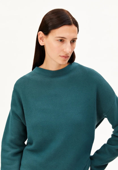 Close-up of the mock neck and fine textured knit on the ARMEDANGELS Canada Merinaa sweater in Petrol Velvet.