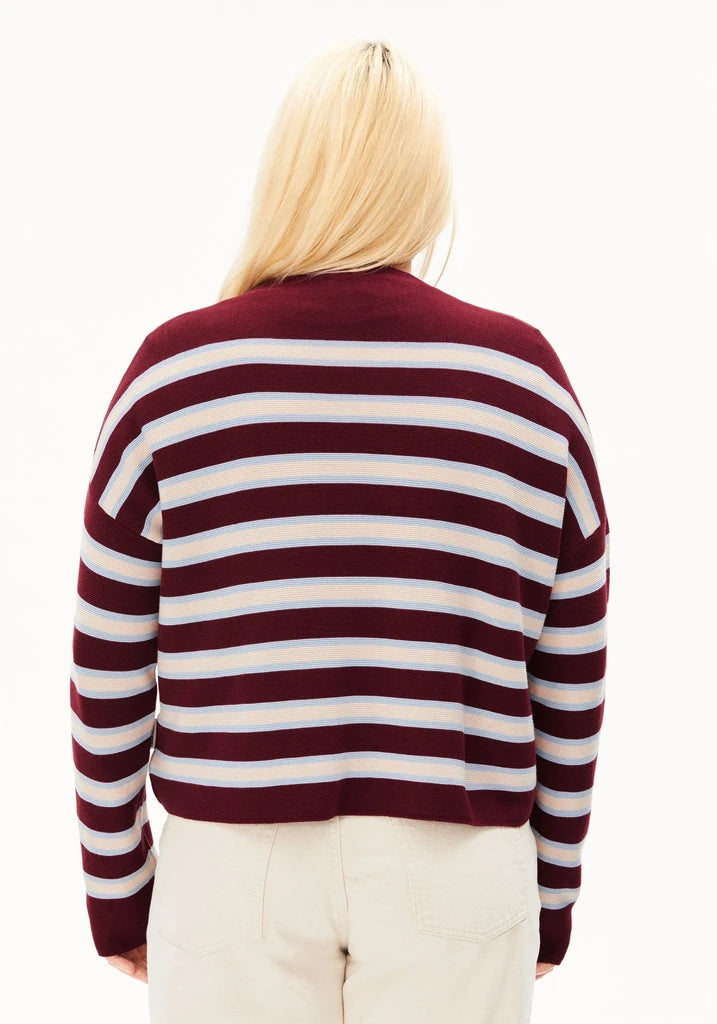 A person viewed from the back wearing a long-sleeve knit sweater with horizontal burgundy and white stripes, paired with light beige pants, against a plain white background.