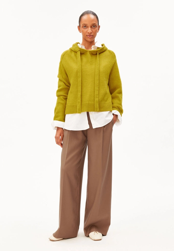 Full-length front view of a woman wearing ARMEDANGELS Canada Mohair-Blend Knitted Hoodie in Mosslace with a white shirt and brown wide-leg trousers, against a white background.