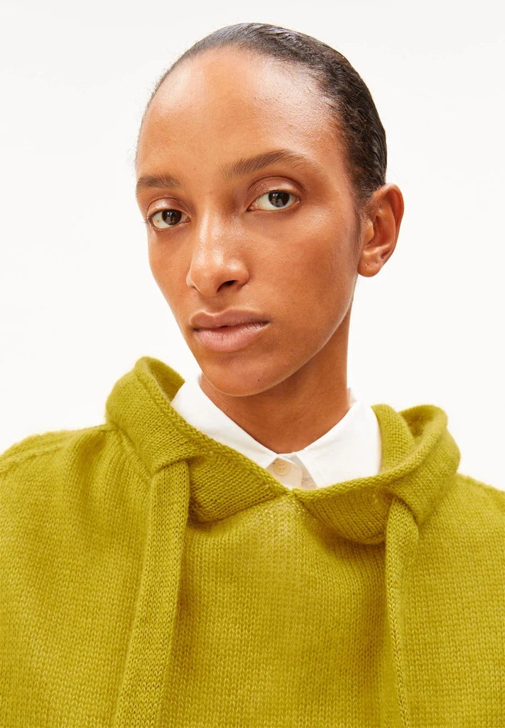 Close-up of a woman wearing ARMEDANGELS Canada Mohair-Blend Knitted Hoodie in Mosslace, showing the hood, tie cords and fluffy knit, against a white background.