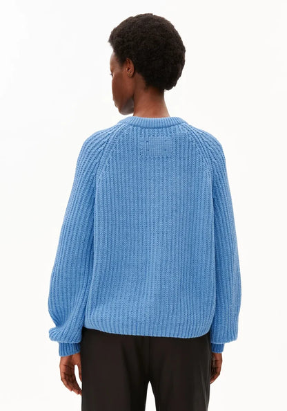 A person shown from the back wearing a light blue ribbed knit sweater and dark pants against a plain white studio background.
