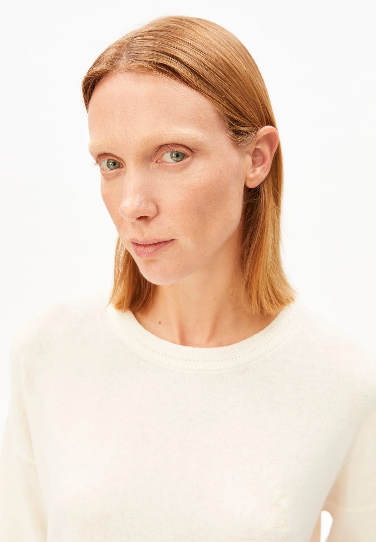 Close-up of the round neckline and fine knit on the ARMEDANGELS Canada Short Sleeve Linen Blend Knit Sweater in undyed cream, worn by a woman against a white background.