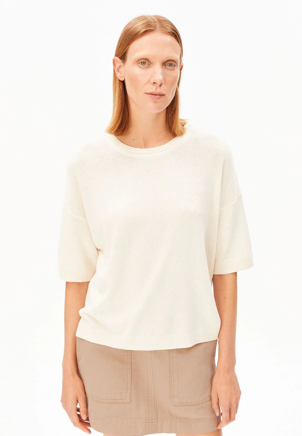 Woman wearing the ARMEDANGELS Canada Short Sleeve Linen Blend Knit Sweater in undyed cream with a tan mini skirt, front view on a white background.