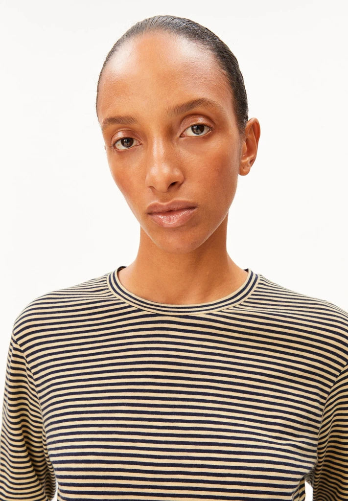 Close-up of a woman wearing ARMEDANGELS Canada Slub Jersey Striped Longsleeve Shirt in Tinted Navy-Golden Hay, showing the round neck and fine stripes, against a white background.