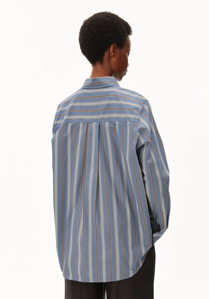 A person shown from the back wearing a light blue striped button-up shirt with thin vertical stripes in brown, orange, and white, paired with dark trousers, against a plain white background.