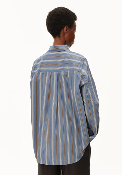 A person shown from the back wearing a light blue striped button-up shirt with thin vertical stripes in brown, orange, and white, paired with dark trousers, against a plain white background.