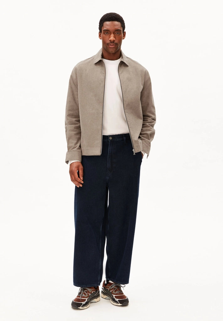 Full-length front view of a man wearing ARMEDANGELS Canada Structured Jacket in Honey Reed open over a white tee, with dark wide-leg jeans and sneakers, against a white background.