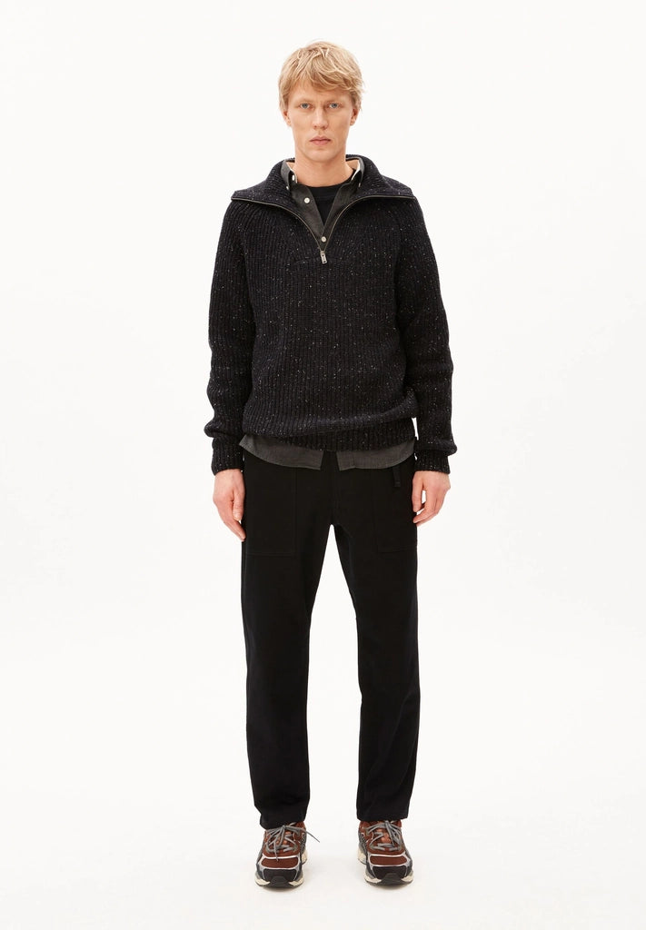 Full-length view of a man in the black ARMEDANGELS Canada Tweed Knit Half-Zip Sweater with black trousers and sneakers on a white background.