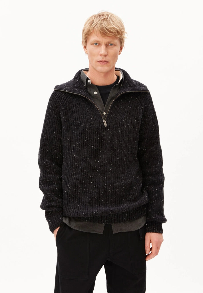 Man wearing ARMEDANGELS Canada Tweed Knit Half-Zip Sweater in black, partly unzipped over a dark shirt, on a white studio background.
