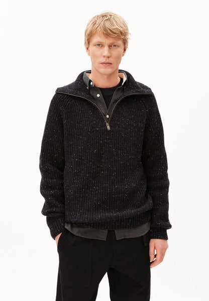 Man wearing ARMEDANGELS Canada Tweed Knit Half-Zip Sweater in black, partly unzipped over a dark shirt, on a white studio background.
