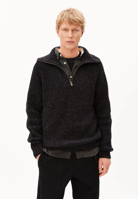 Man wearing ARMEDANGELS Canada Tweed Knit Half-Zip Sweater in black, partly unzipped over a dark shirt, on a white studio background.