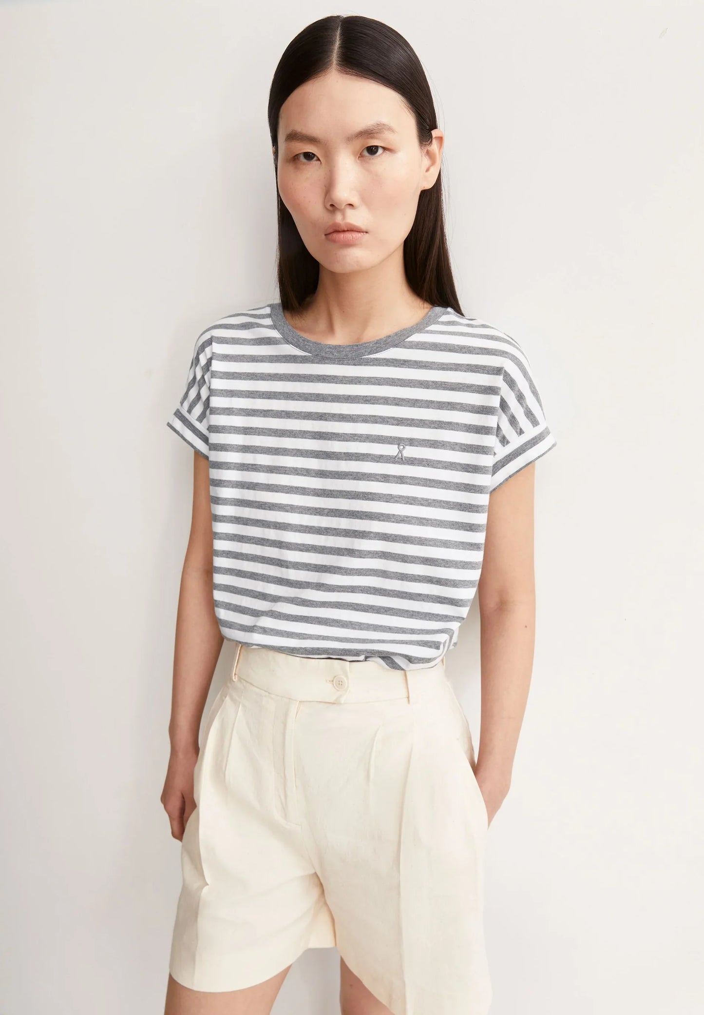 Woman wearing a striped t-shirt and beige shorts against a plain background