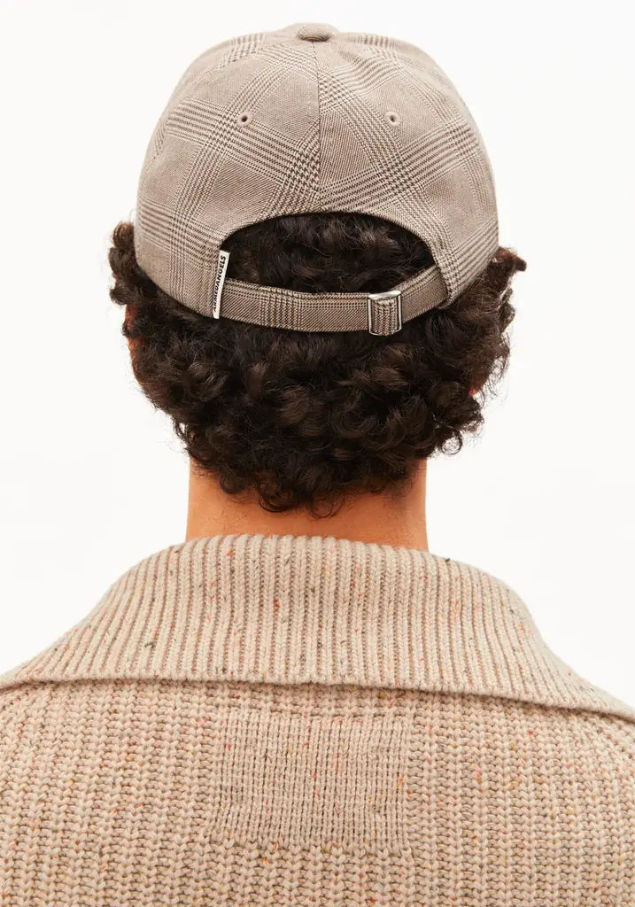 Back view of a person wearing a beige plaid baseball cap and a matching beige knit sweater against a plain white background.