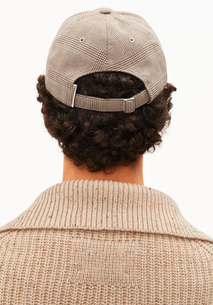 Back view of a person wearing a beige plaid baseball cap and a matching beige knit sweater against a plain white background.