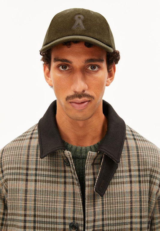 Man wearing ARMEDANGELS Canada Yenaas Cord Cap in Dark Earth with a plaid jacket, front view against a white background.