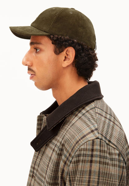 Side profile of a man wearing ARMEDANGELS Canada Yenaas Cord Cap in Dark Earth, showing the curved brim, against a white background.