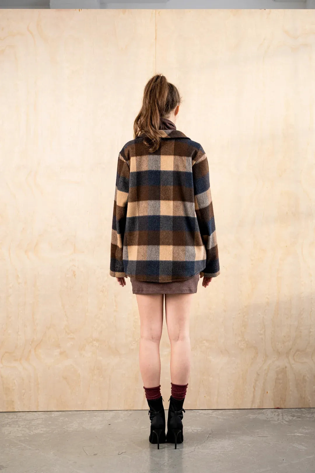 Back view of the BodyBag by Jude Barrington Overshirt in Plaid Quatro, showing the boxy plaid back, dropped shoulders and straight hem over a brown mini dress.