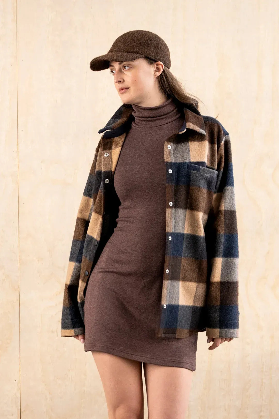 Close-up of a woman wearing the BodyBag by Jude Barrington Overshirt in Plaid Quatro, showing the brushed plaid wool blend, the snap buttons and the chest pocket, styled with a brown wool cap.
